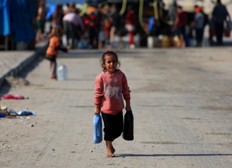 یک دختر فلسطینی در شهر غزه، در بحبوحه قطع تقریباً کامل آب آشامیدنی، ظرف‌های آب را حمل می‌کند.