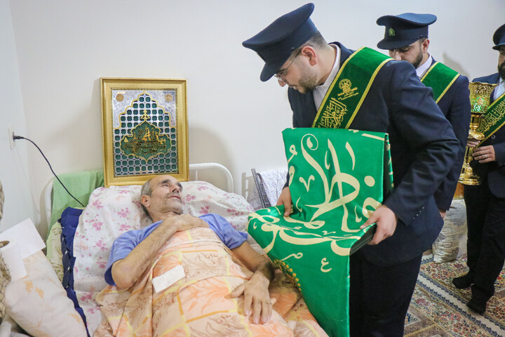 عیادت از جانباز قطع نخاعی جنگ رمضان به مناسبت روز ولادت حضرت رضا علیه السلام با حضور خادمان و پرچم متبرک حضرت معصومه سلام الله علیها